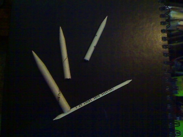 Three gray tortillons of different sizes and a small stump on a black hardback sketchbook cover, photo by Robert Sloan.